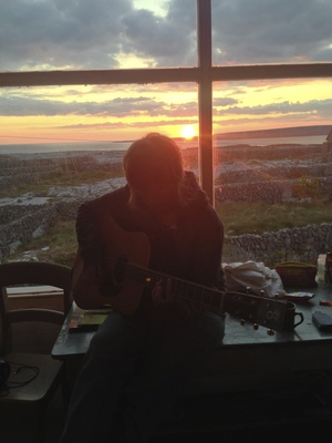  Klay playing guitar in front of the huge window with the sunset at her back. 